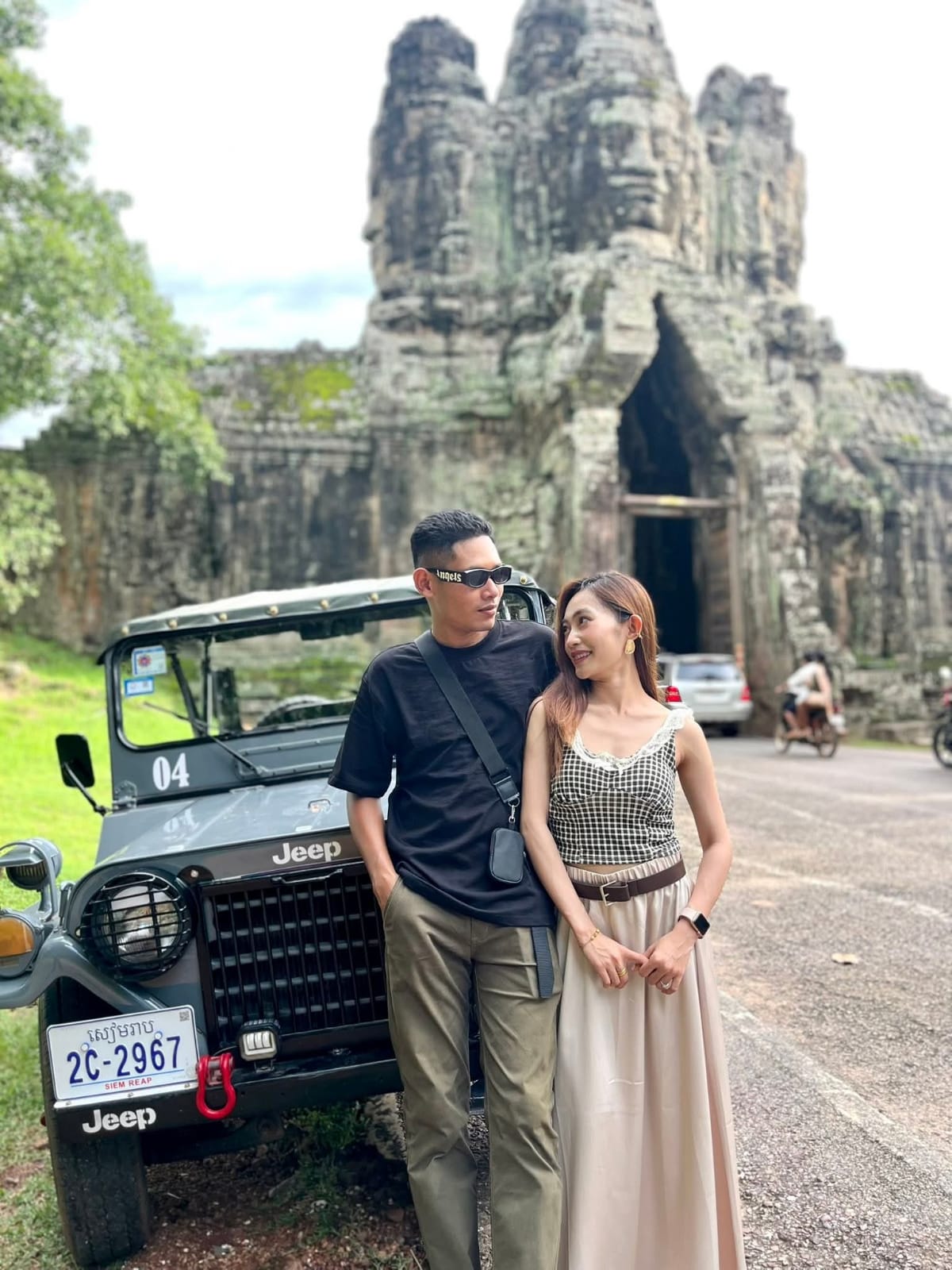 Couple posing with vintage Jeep at Bayon temple gate, Angkor, Siem Reap