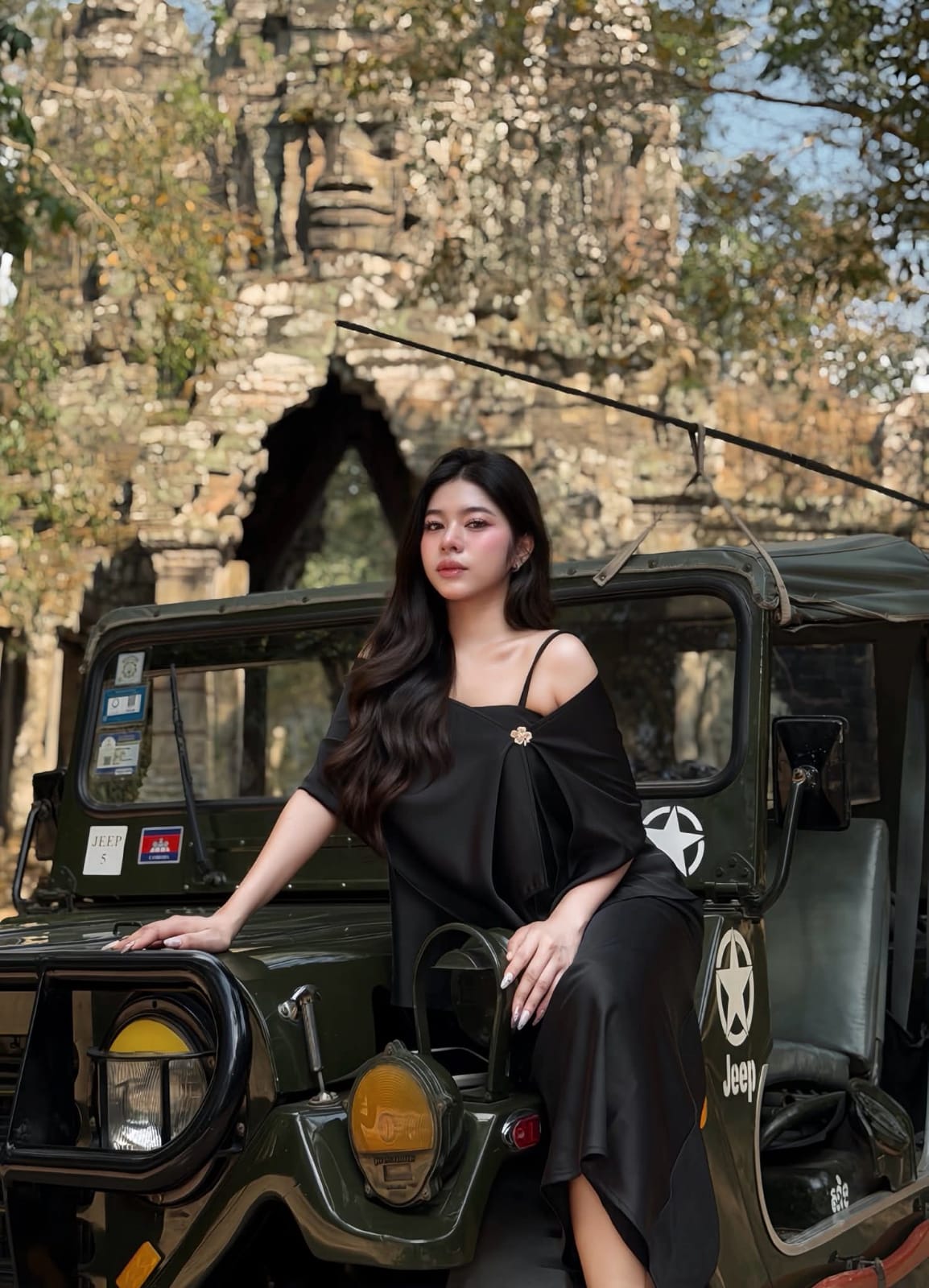 Woman sitting on vintage Jeep hood at a Khmer temple, Siem Reap